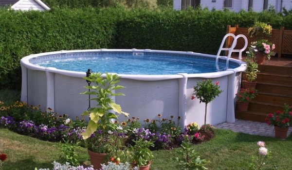 Piscina fuori terra bianca abbellita con fiori e soppalco per ingresso.