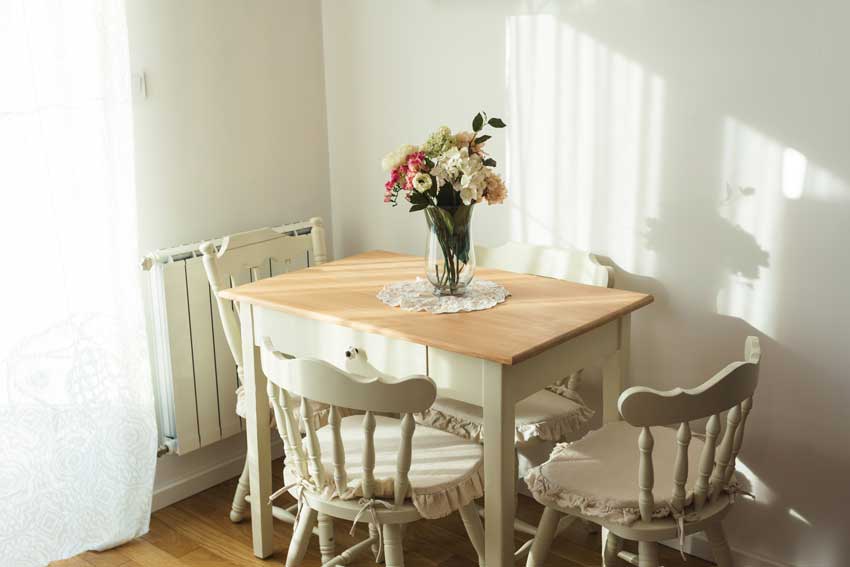 piccola sala da pranzo con arredamento shabby chic, tavolo con top in legno e vaso centrale.