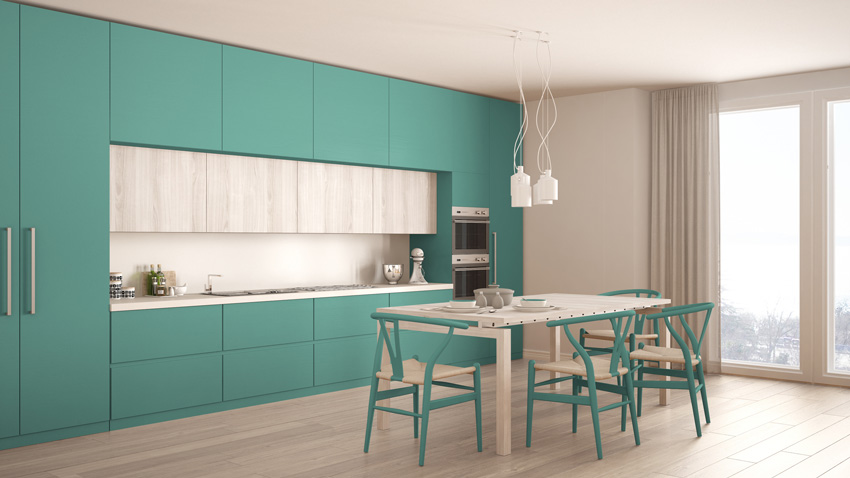 cucina di colore turchese con un tocco di grigio chiaro, tavolo in legno con sedie design abbinati ai mobili turchesi.