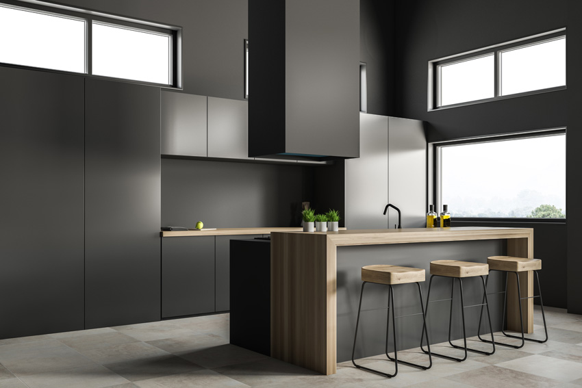 cucina affascinante di colore nero con isola e top in legno, cappa sospesa nera.