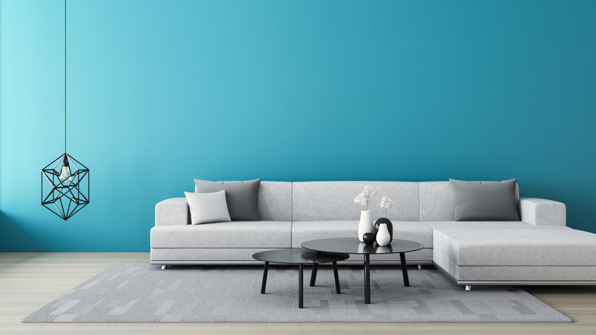 soggiorno con divano ad angolo grigio e parete color azzurro, lampadario design a sospensione.