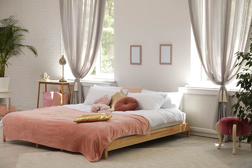 Camera da letto con coperta rosa e tende color tortora.