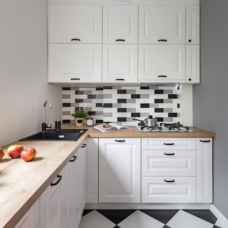 Piccolissima cucina bianca ad angolo con top in legno e piastrelle tipo mosaico bianco e nero.