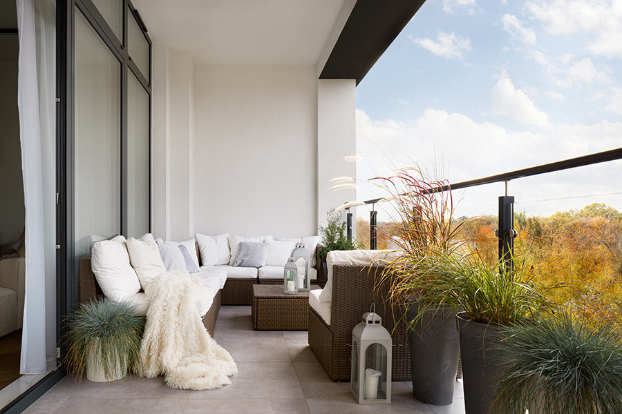 Balcone con divano da esterno ad angolo decorato con vasi di fiori.