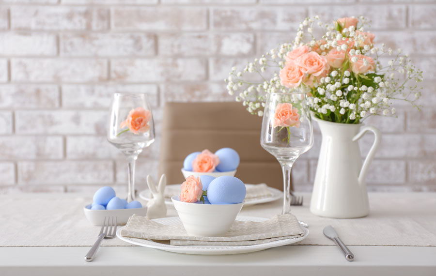 Tavola pasquale con ciotole bianche e ovetti celesti, vaso di fiori bianchi e rose. 