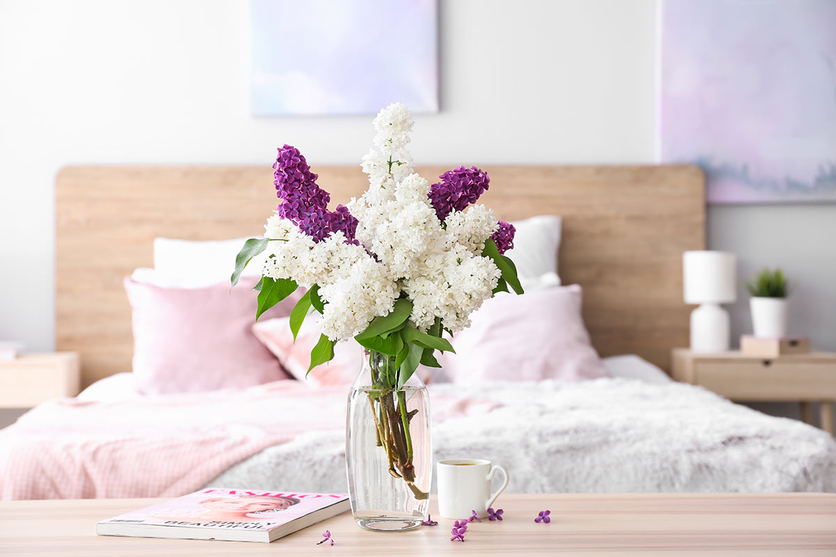 Vaso in vetro con fiori di lilla bianchi e fucsia sul tavolo in camera da letto.