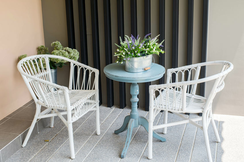 Piccolo terrazzo arredato in stile shabby chic con sedie bianche di vimini e tavolino rotondo celeste effetto invecchiato.