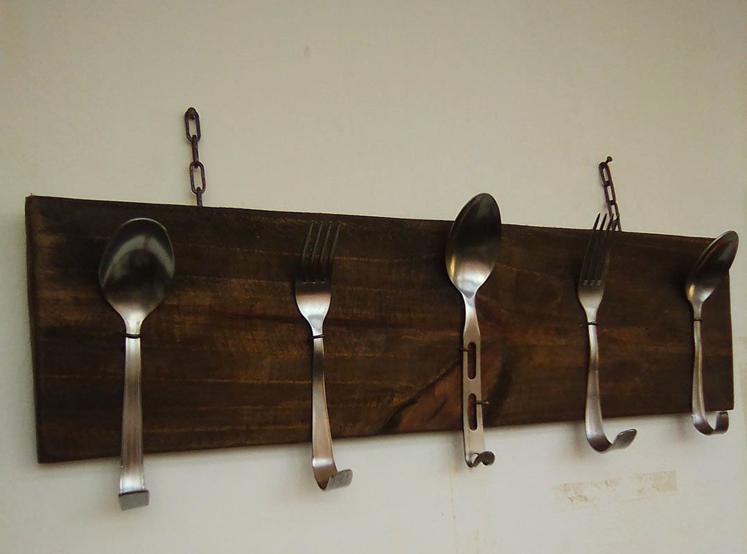 Appendiabiti realizzati con forchette e cucchiai fissati su una tavola di legno di pallet.