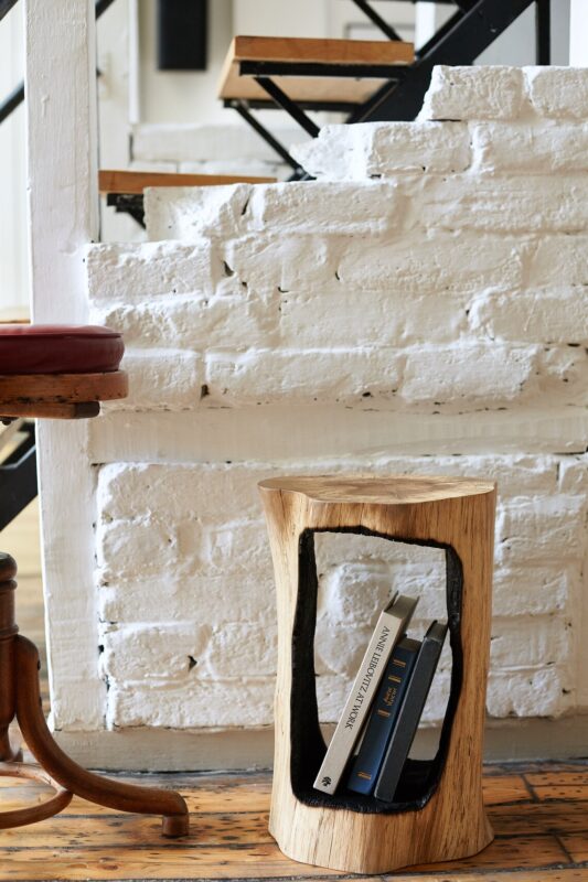 Small floor side table with organic shape made of burnt hardwood material on a wooden floor close to a white brick wall