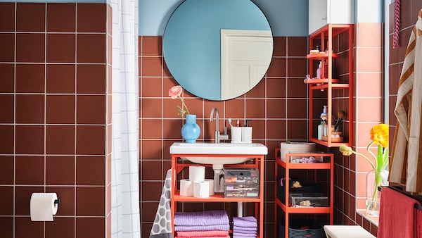 Bagno colorato con mobile per lavabo, scaffale e carrello in acciaio rosso-arancione e specchio rotondo.