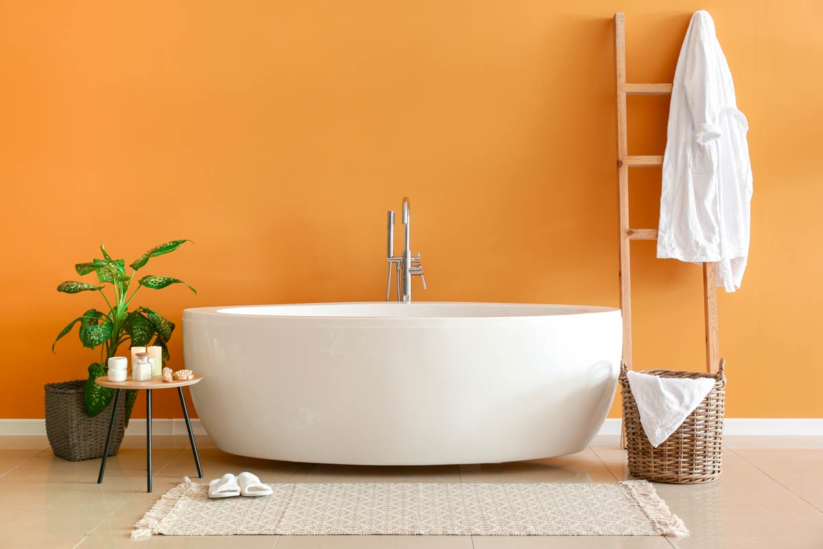 Colore arancione pareti bagno con vasca bianca.
