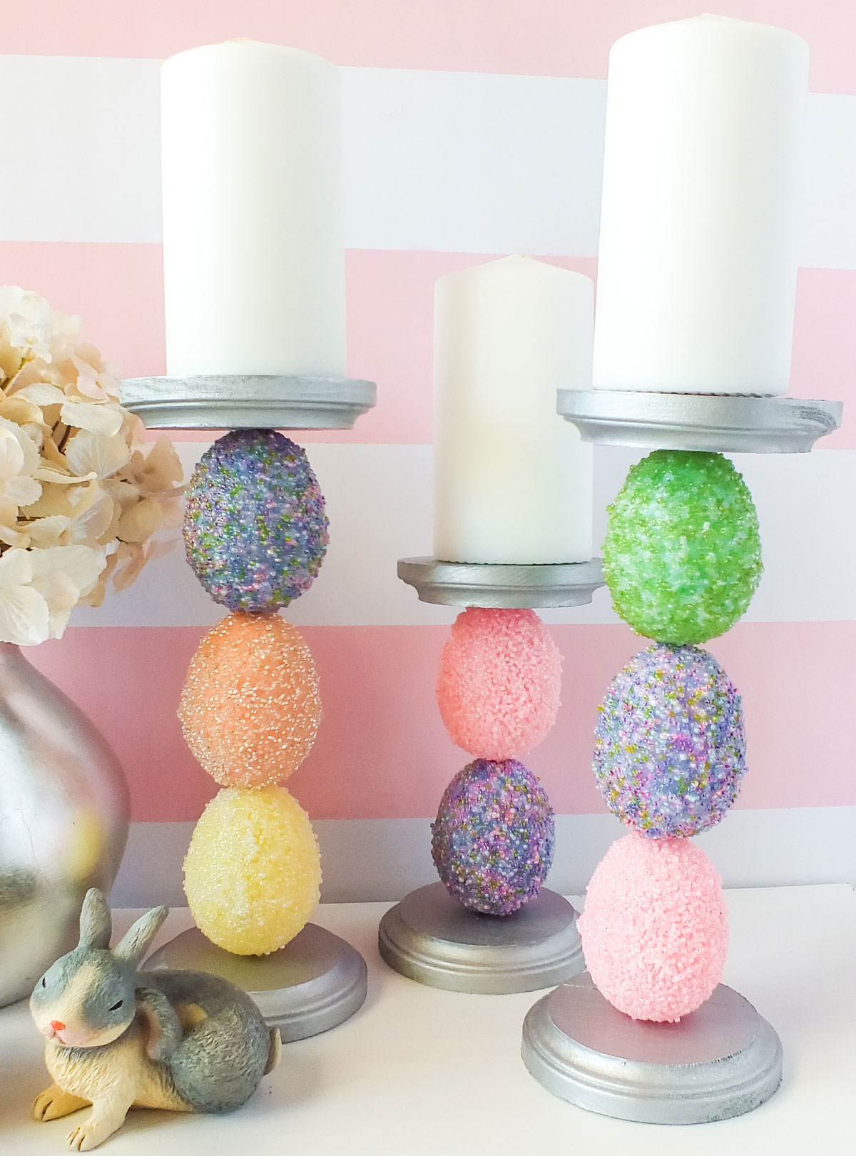 Closeup of three DIY Beaded Easter Egg Candle Holders sitting on a white surface in front of a pink and white background.