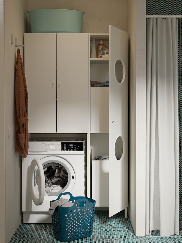 Mobile bianco per lavatrice, lavatrice, mobile per lavanderia con due fori sull'anta, pavimento a piastrelle verdi.