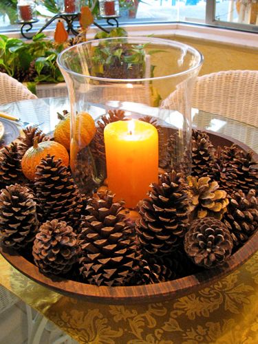 Centrotavola fai da te con pigne e candela arancione, ideale per l'autunno.