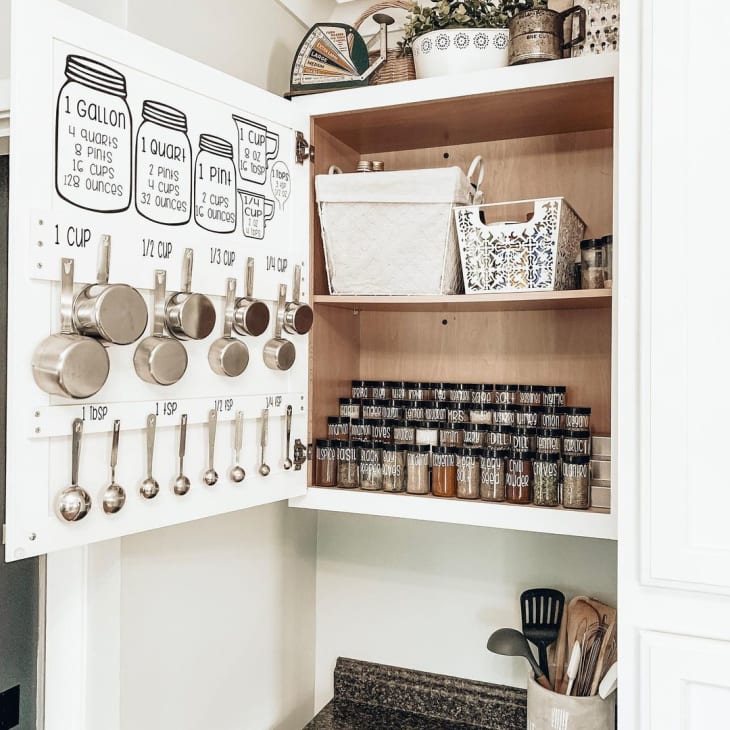 opened spice cabinet, with hooks installed on the inside of the door to hang measuring cups and spoons