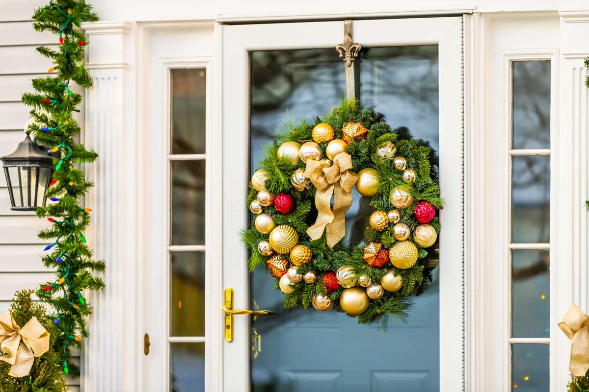 Fuori porta natalizio con ghirlanda di pino e palline di natale dorate e rosse.