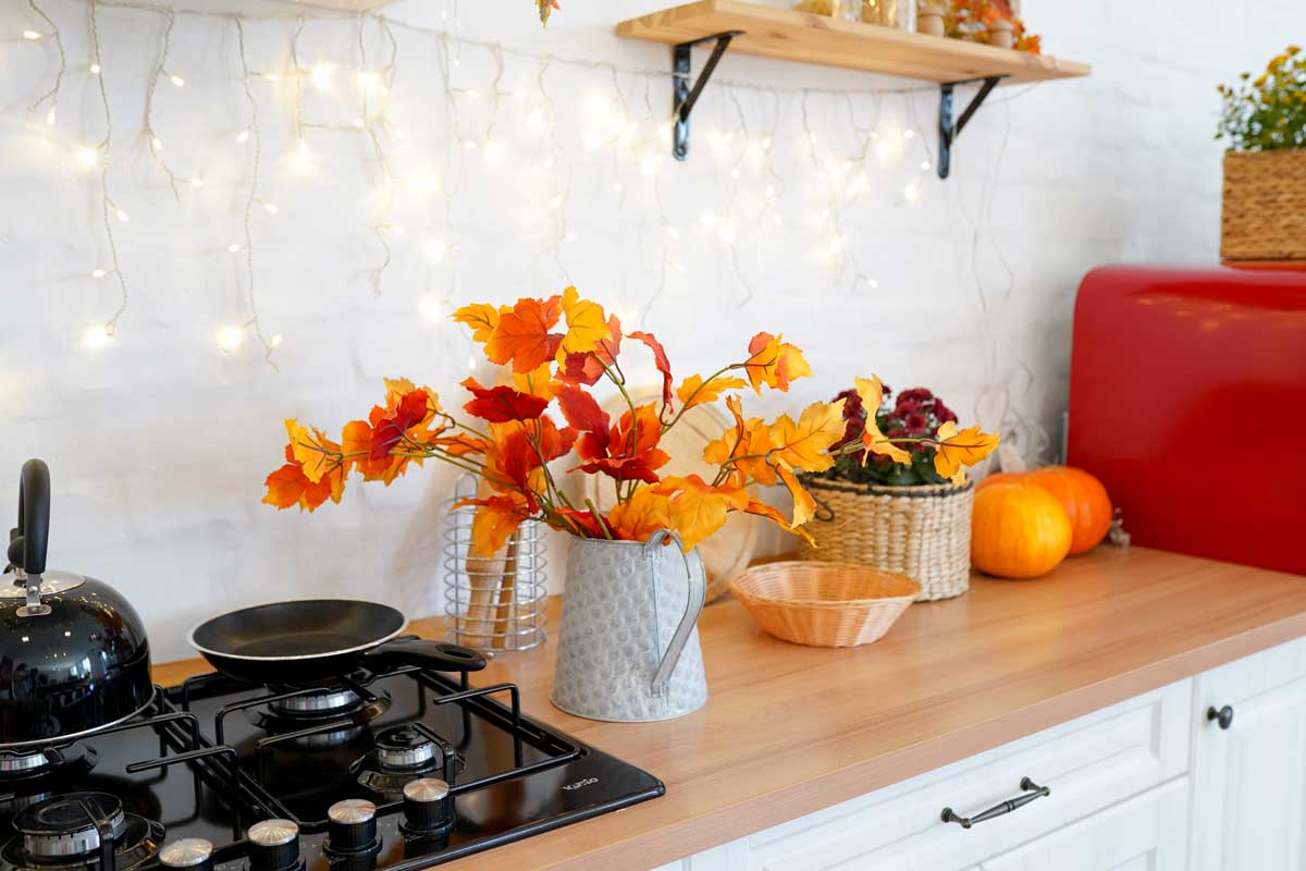 Vaso con fiori autunnale poggiato su mobile in cucina.