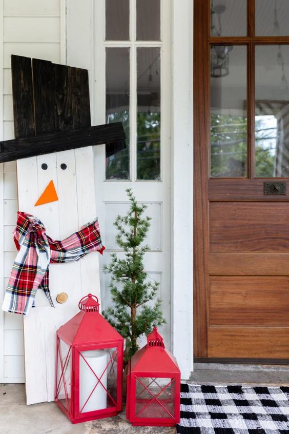 Alberello, pupazzo di neve in pallet e lanterne rosse sotto al portico durante il Natale.
