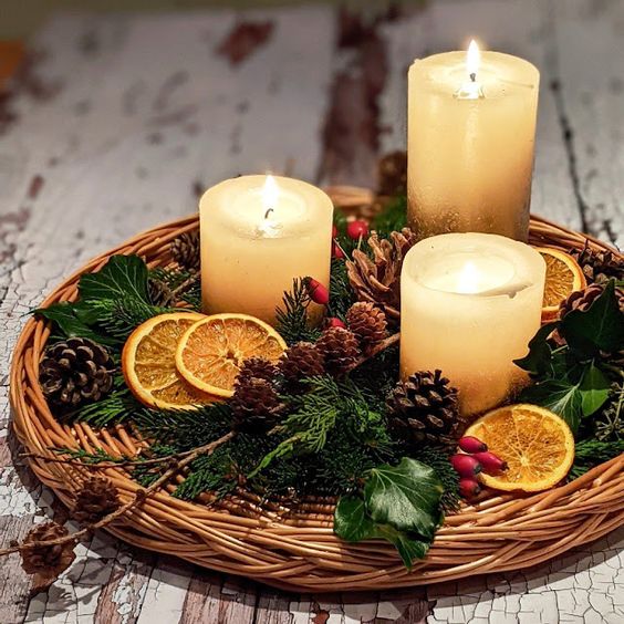 Centrotavola natalizio con arance, pigne e candele in cesto di vimini.