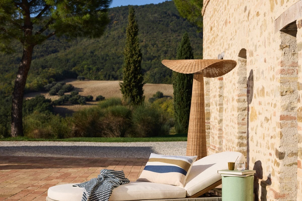 Area relax esterna con lampada Leni in rattan vicino alla parete in pietra