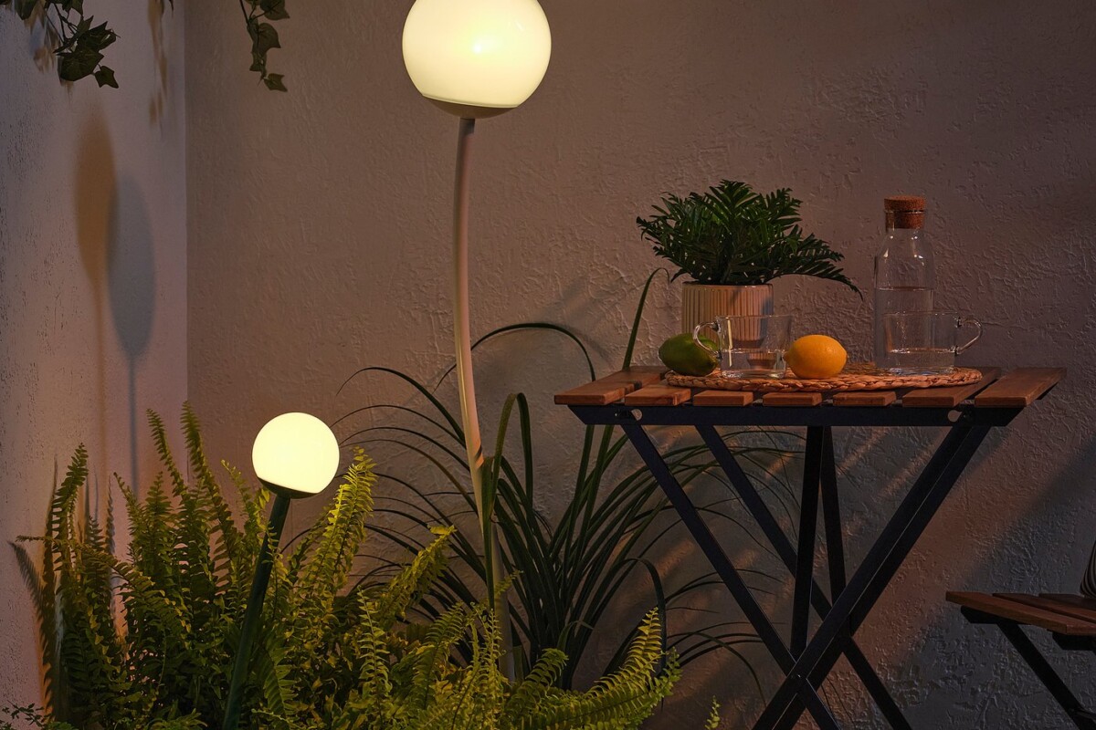 Lampada solare IKEA SOLVINDEN accesa tra piante e tavolino da balcone