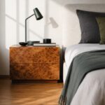 Comodino in radica accanto a un letto contemporaneo con tessili verdi e grigi