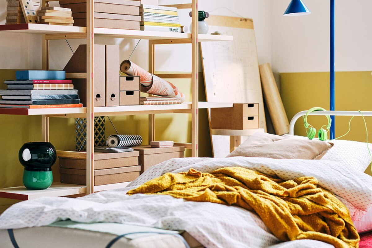 Scaffale IKEA PS 2026 accanto al letto con ripiani aperti e oggetti ordinati