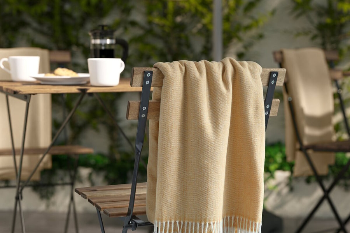Plaid IKEA HOLMVI beige giallo con frange appoggiato su una sedia in legno