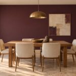 Sala da pranzo con parete color melanzana opaca, tavolo in rovere e sedie color avorio