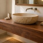 Lavabo ovale in pietra arenaria beige su mobile sospeso in noce in un bagno bianco